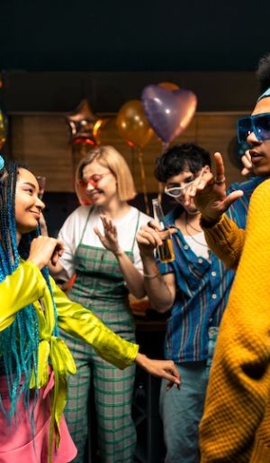 Group of friends making party at home on new year evening. Young women and men celebrating in the apartment drinking and eating, dancing and having fun. Concept about holidays and parties.